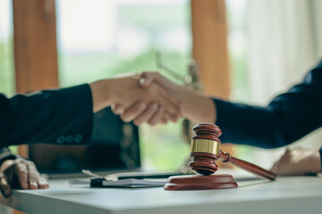 Fototapeta na wymiar Close-up view of a lawyer holding a client's hand, making an agreement, signing a contract, a side judge's hammer and brass scales. Law offices, law and justice consulting services