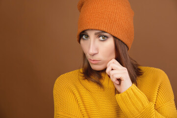Portrait of a beautiful pensive brunette woman, wearing a yellow sweater and an orange hat