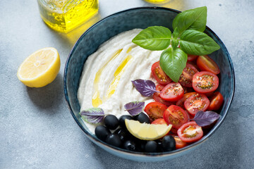 Bowl of taramasalata or greek fish roe dip served with cherry tomatoes, black olives and basil, studio shot on a light-blue stone background