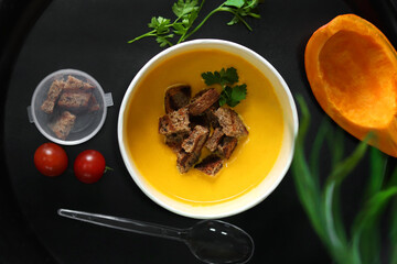 Pumpkin soup with pulled bread in a round eco takeaway container on a black background. Healthy food delivery concept.	