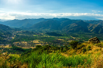 mountain valley sunset, view from green hill to a highland plato with blue mountains and beautiful cloudy sunset on the background