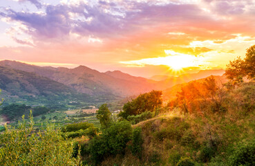 mountain valley sunset, view from green hill to a highland plato with blue mountains and beautiful cloudy sunset on the background