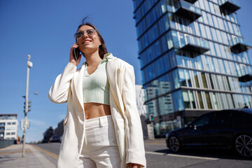 Smiling young woman in white suit calling friend stand near business centre