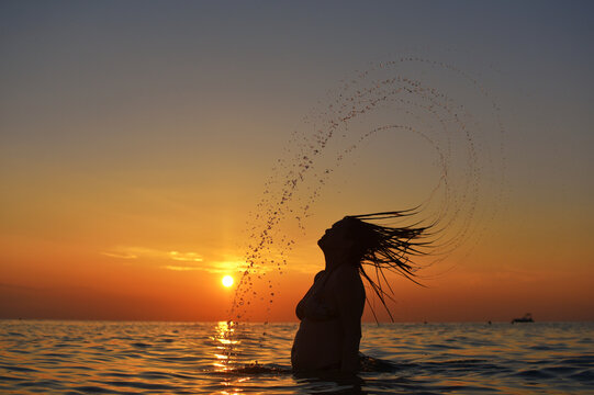 Beautiful woman throwing back her hair into the water at the beach. Silhouette of hair and water at sunset. Summer vacation concept