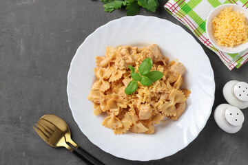 Pasta farfalle with turkey in tomato-sour cream sauce, served cheese and basil on white plate on gray background