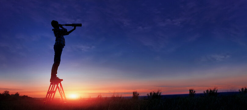 The child looks at the stars through a telescope. A teenager boy looks at the night sky through a spyglass against the backdrop of a sunset while in the field.