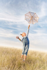 Child plays in a field on a summer day. Little girl with a bouquet of flowers and an umbrella against the blue sky. Cheerful and happy kid dreams of flying.