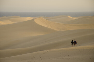 Fototapeta na wymiar Two men walking in the Maspalomas Dunes. Natural Reserve of the Maspalomas Dunes. San Bartolome de Tirajana. Gran Canaria. Canary Islands. Spain.