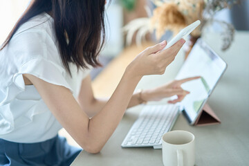 PC画面を前に、スマートフォンを操作する女性