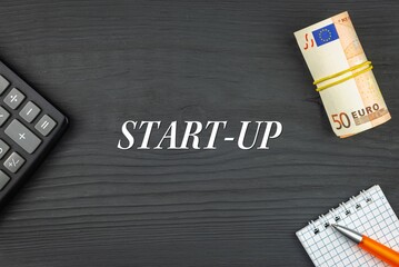START-UP - word (text) and euro money on a wooden background, calculator, pen and notepad. Business concept (copy space).