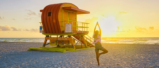 Obraz premium Asian women doing yoga during sunrise on the beach at Miami Florida South Beach. people doing yoga in the morning