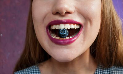 A woman eats blueberries. A berry in a woman's mouth. Cropped view.