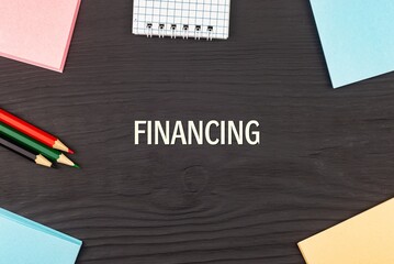 FINANCING - text, stickers and colored pencils on a black wooden table. Business concept: buying, selling, commerce (copy space).