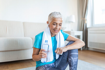 Senior woman holding plastic bottle of water,wiping sweat with a towel, exhausted after the daily...