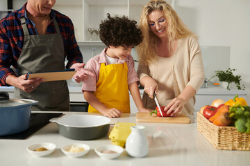 Father and son looking at smiling mother cutting vegetables for salad