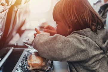little candid kid boy five years old eats burger or sandwich food sitting in airplane seat on flight traveling from airport. children take a bite. child in air plane eating lunch or dinner meal. flare