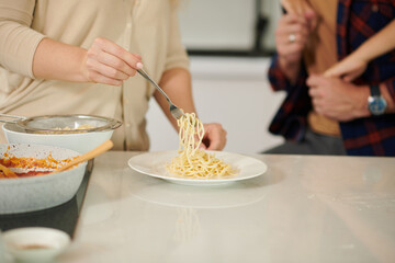 Closeup image of woman putting pasta in plates for her husband and son