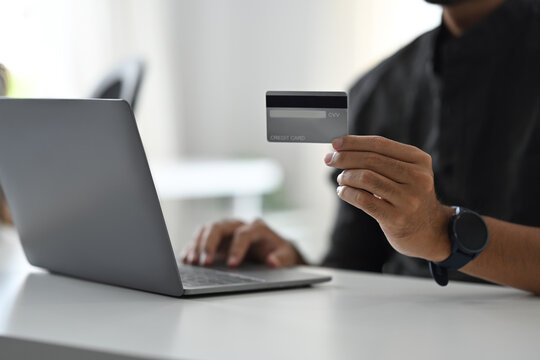 Cropped view of man holding credit card and using laptop for making payment online. Online shopping, e-commerce concept