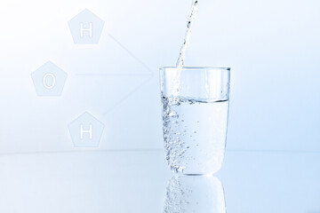 Pouring cristal cleen water into glass, on blue background, close up. Hologram with letters H and O
