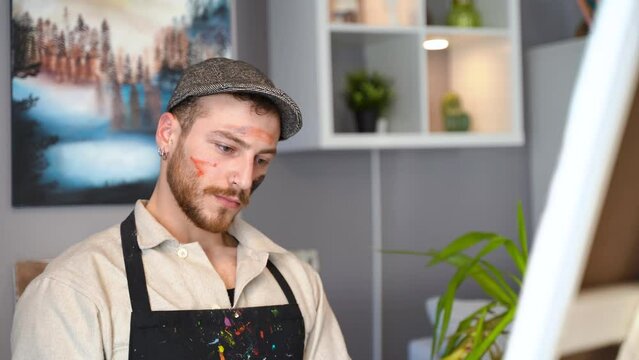 Painter's face while painting. 
While painting, the painter wipes his forehead and his face is smeared with paint. Artist outfit and paints.
