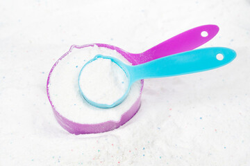 Laundry detergent for washing machines and a plastic scoop for dosing. Washing powder with measuring spoon. White wash powder with with colored granules
