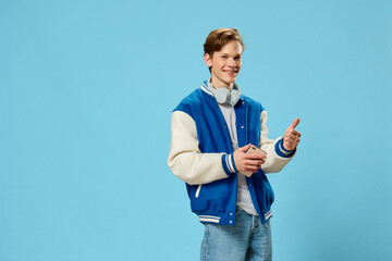  young stylish guy in a bomber and jeans stands with a phone in his hands and headphones around his...