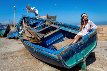 A beautiful girl sits in a blue boat against a blue sky with seagulls. Essaouira. Morocco