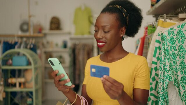 African american woman customer holding shopping bags using smartphone and credit card at clothing store