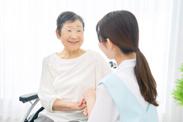 Fototapeta premium 介護施設で車椅子に乗るシニア女性と会話する介護士