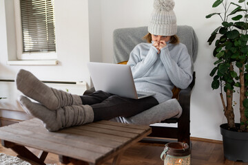 A woman in warm clothes with laptop. Low heating temperature in the house. Energy crisis concept	