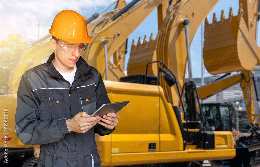 Aufkleber Engineer in a helmet with a digital tablet on the background of construction machines