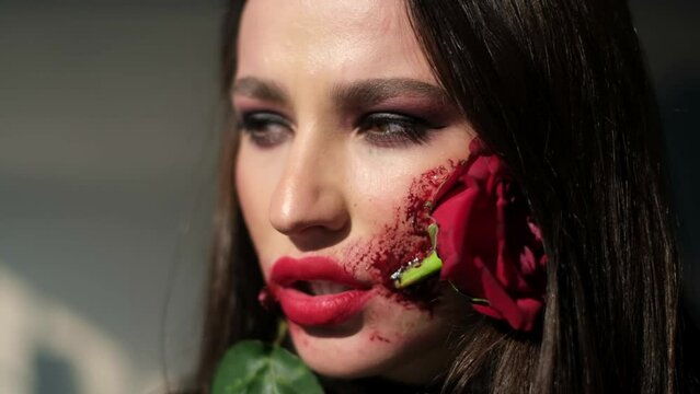 Glamorous brunette woman with makeup for Halloween, rose flower in her mouth. High quality 4k video