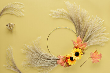 Floral wreath from dry pampas grass and Autumn leaves on golden paper. Flat lay, top view with...