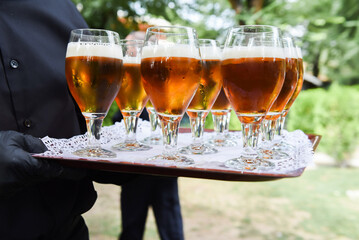 Waiter serving several beers in glasses on a tray to guests at an event, wedding, party, etc.