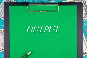 OUTPUT - word (text) and money bills, dollars on a green background notepad, pencil, wooden table. Business concept: buy, sell, commerce (copy space).