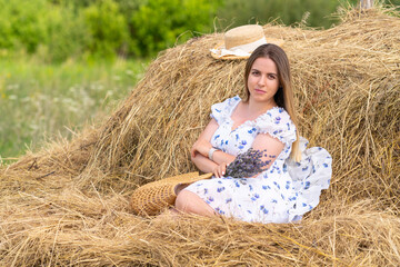 Young woman sitting on hay rick in summer