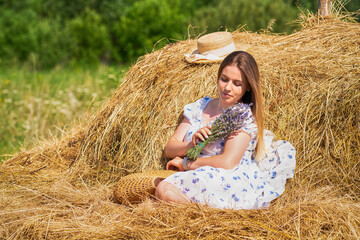 Pretty young woman posing with lavender flowers on fresh hay