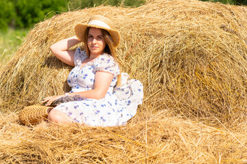 Pretty young fashion model posing on a hay rick in summer