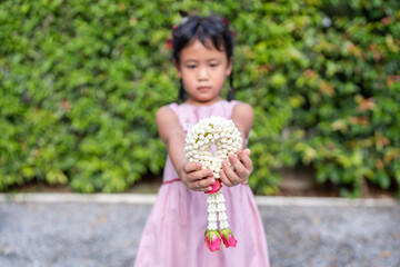 Small girl holding jasmine garland in her hand and gives to her mother on Thai Mother day. 