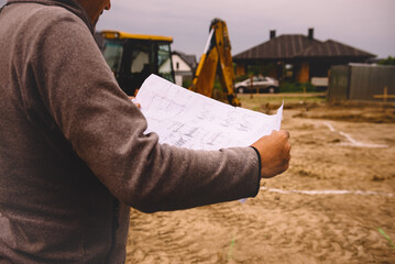 Architect showing house build plans at the building site. Engineer working with blueprints outside on construction site