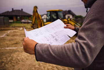 Architect showing house build plans at the building site. Engineer working with blueprints outside on construction site