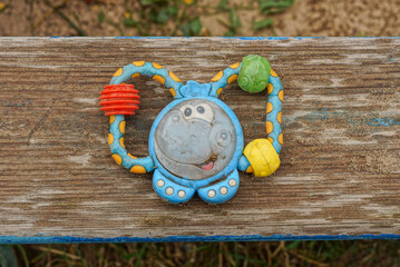 one plastic colored small dirty toy rattle lies on a gray wooden table board outdoors