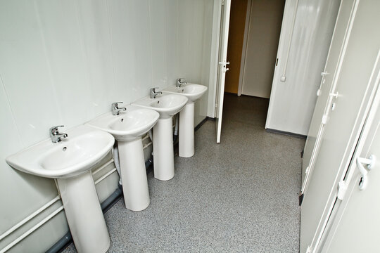 Public toilet. Sinks installed in row. Doors to toilets are closed. Toilet in public facility. Lavatory room with cubicles and washstands. Public bathroom without anyone. Sinks installed along wall