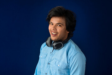 Portrait of a handsome young man enjoying music on headphones on blue background.