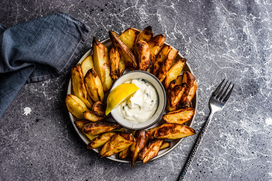 Close-up of a plate of baked potato wedges with sour cream, garlic and dill dip