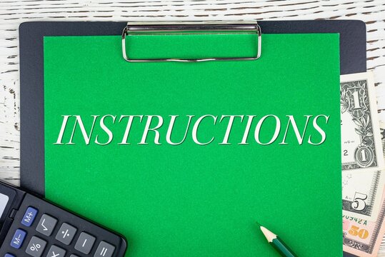 INSTRUCTIONS - word (text) dollar bills on green background, pencil, calculator and wooden white table. Business concept: buying, selling, commerce (copy space).