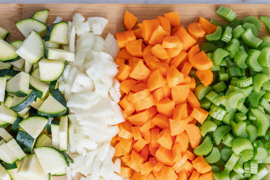 Overhead view of chopped courgette, onion, carrot and celery on a wooden chopping board