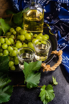 Bottle and two glasses of Georgian chacha brandy on a table with a bunch of green grapes and traditional Georgian tablecloth