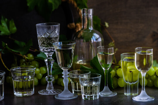 Bottle and assorted glasses of Georgian chacha brandy on a table with bunches of green grapes