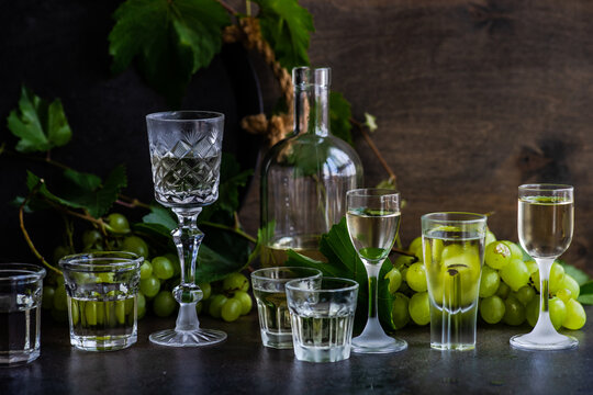 Bottle and assorted glasses of Georgian chacha brandy on a table with bunches of green grapes
